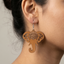 Light brown wooden elephant dangle earrings featuring an intricate laser-cut mandala design on the forehead, hanging from a silver metal hook, worn by a woman.