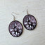 The Addams Family wooden earrings for women featuring Wednesday, Gomez, Morticia, Uncle Fester, Pugsley, Lurch, Grandmama, and the family in a monochrome oval design.