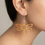 Dark wooden dragonfly dangle earrings featuring intricate floral cutouts, hanging from a standard metal hook, worn by a woman.