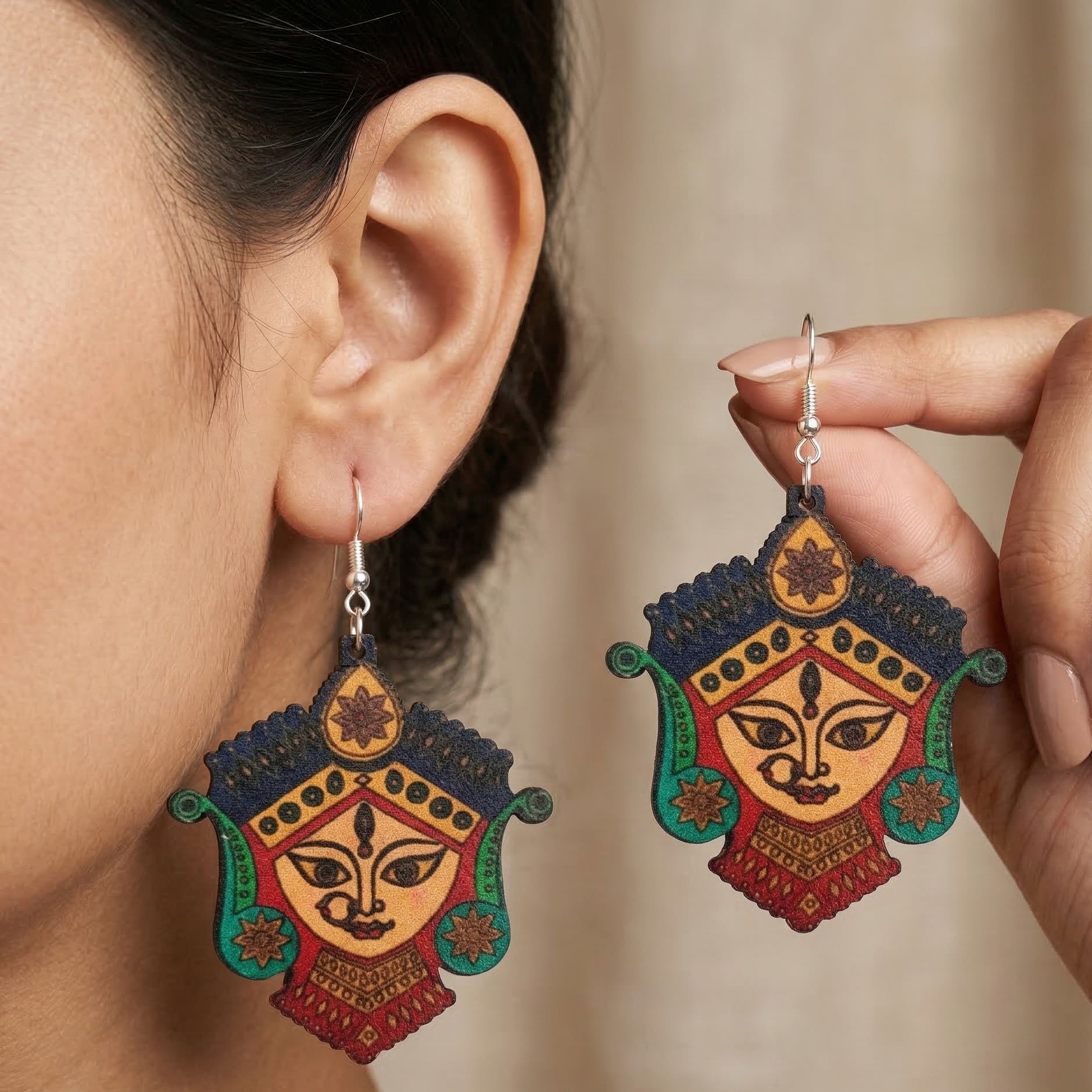 Woman wearing vibrant, colorful wooden dangle earrings featuring a traditional painted design of Goddess Durga's face.