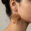 Light brown wooden elephant dangle earrings featuring an intricate laser-cut mandala design on the forehead, hanging from a silver metal hook, worn by a woman.