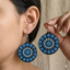 Woman wearing round wooden dangle earrings featuring an intricate blue, white, and black dot art mandala design.